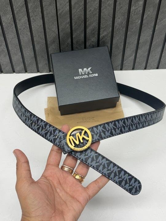 Michael Kors black monogram belt with a silver logo buckle, displayed next to its original square MK gift box and white drawstring dust cover.